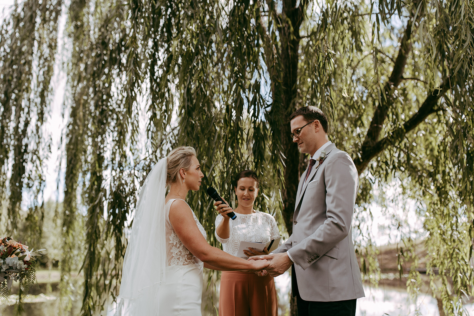 Bride and groom exchanging wedding vows under willow tree