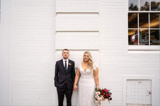 Bride and Groom standing against white brick wall
