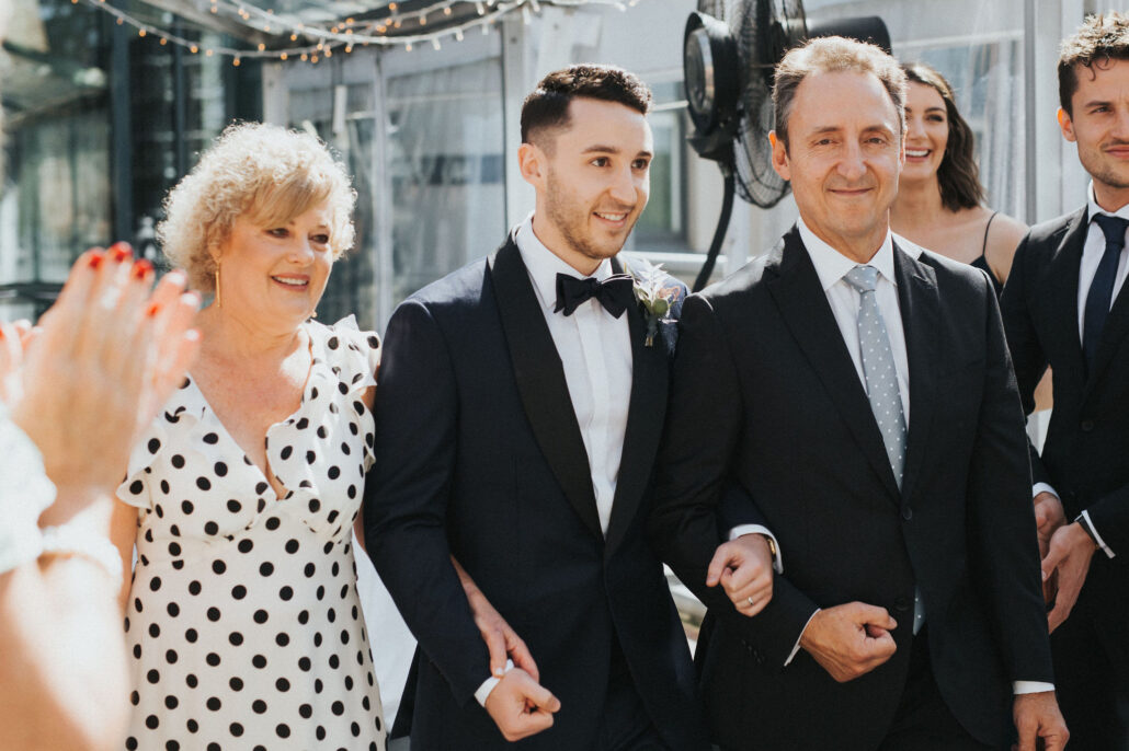 Groom makes entrance with parents at wedding