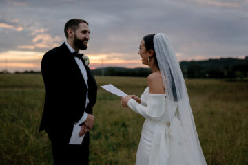 Bride and groom sharing marriage vows in a field at sunset
